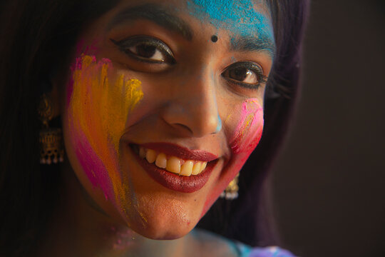 A YOUNG WOMAN LOOKING AT CAMERA AND SMILING WITH GULAL ON HER FACE	