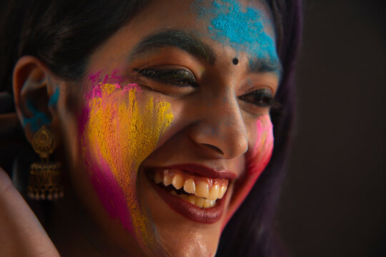 A YOUNG WOMAN WITH GULAL ON HER FACE LOOKING AWAY AND LAUGHING	