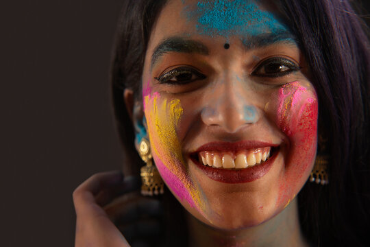 A HAPPY YOUNG WOMAN SMILING AND LOOKING AT CAMERA WHILE PLAYING HOLI	