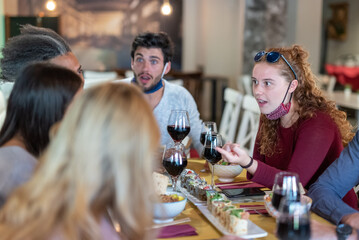 stunned expression of young people at restaurant, group of friends eating and drinking red wine in outbreak time of Corona Virus, social gathering and facemasks