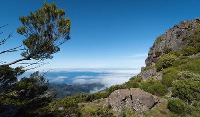 Fototapeta na wymiar Above the clouds on a mountain trail. Colorful mist in valley. Trekking from Pico do Arieiro to Pico Ruivo, Madeira island, Portugal. 
