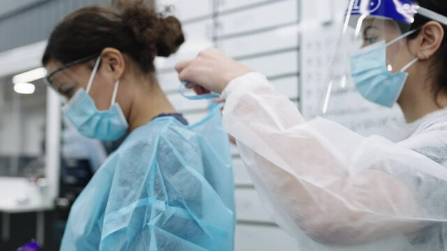 Nurse In Face Shield Tying Scrubs Of Doctor