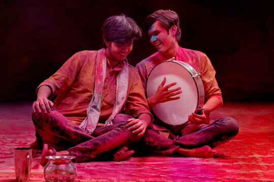 TWO YOUNG MEN SITTING TOGETHER AND ENJOYING HOLI CELEBRATIONS BY SINGING AND PLAYING DAFLI	