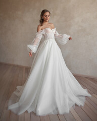 Fototapeta premium Full length bride portrait. Elegant woman in white wedding dress spinning in beige interior. Dynamic shot. Elegant female model standing and posing in ball gown