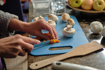 women's hands cut carrots on a blue chopping board