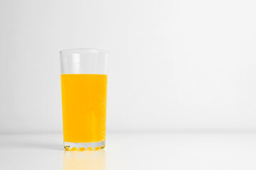 Glass of carbonated juice standing on table indoors. Light background, copy space