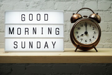 Good Morning Sunday word in light box and alarm clock on wooden shelves