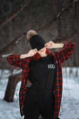 a European girl with red hair stands on the street in winter and covers her face with a hat