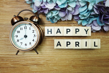 Happy April alphabet letters with alarm clock on wooden background