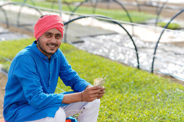 Young indian farmer counting and showing money at greenhouse