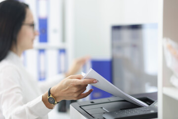 Young woman pulling paper out of printer closeup. Replacement of cartridges and repair of office equipment concept