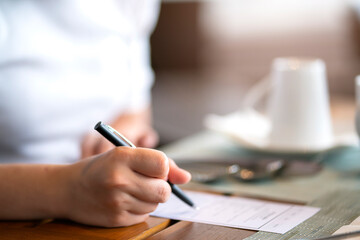 Closeup image of a hand writing on blank notebook or paper order filling form with coffee cup on table in cafe