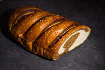 Unusual two-color fresh loaf of bread on a black background, photo in a low key in hard light,...