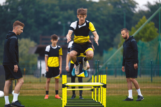 Youth Soccer Team on Training. Young Boys in Football Club Practicing Durability. Teenage Boy Jumping High Over Hurdle Obstacles. Young Men Coaching Sports Team on Practice Field. Youth Soccer School