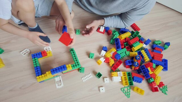 Family and childhood concept. Father and son play together and create colorful house of plastic blocks