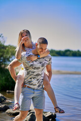 The man carries his girlfriend on his back across the stream. The woman laughs merrily. vertical