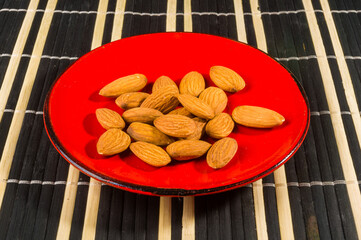 Almonds nuts in a red saucer on a bamboo mat, closeup