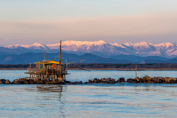 Trebuchet fishing hut at sunset, against the Alps covered with snow, Marina di Pisa, Tuscany, Italy