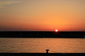 Fototapeta na wymiar Sole sorgente da dietro il bastione del porto di Riposto
