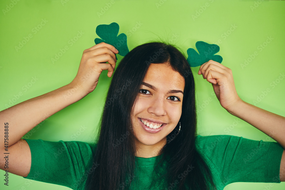 Wall mural modern girl holding a shamrock on an isolated green background. happy st patrick's day.