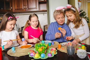 Blonde mom shows her daughters how to decorate Easter eggs at home in the kitchen