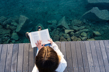 View from top of young school student sitting on a pier on the transparent blue ocean or sea water...