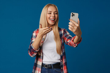 Cheerful blonde girl gesturing while taking selfie on smartphone
