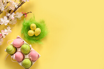 Easter pastel eggs in carton box and spring blooming flowers on yellow. View from above. Copy space.