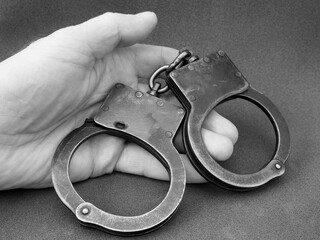 Police handcuffs in a man's hand, a black-and-white photo on a dark background. The concept of the...