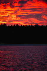 Red sunset with clouds over lake in forest in Russia