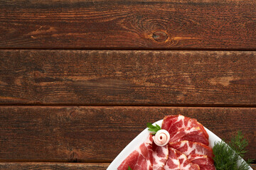 Slices of Prosciutto di Parma ham and fresh vegetables on a wooden table. Copy space