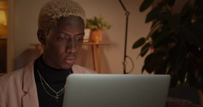 Close up view of handsome man typing and using laptop while sitting on sofa.Concentrated afro american young guy with dyed hair browsing internet at home. Concept of leisure