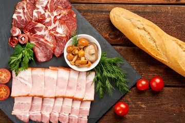 Close-up of sliced deli meats with vegetables and baguette on a slate board.