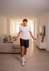 handsome young man doing exercises at home with jump rope during quarantine