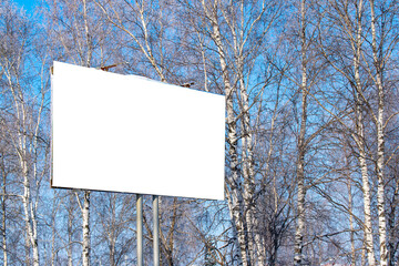 Billboard on the street in the city with an empty white space for text on a background of trees in frost, snow, blue sky, beautiful winter background, mock up