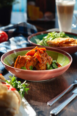 Appetizing meat goulash with sauce (meat and vegetables), carrots and cilantro on the table in a beautiful setting, sunny lighting