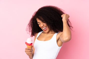 Young african american woman holding a cornet ice cream isolated on pink background celebrating a victory