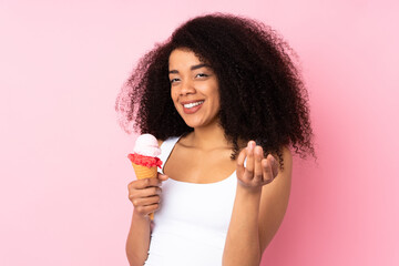 Young african american woman holding a cornet ice cream isolated on pink background inviting to come with hand. Happy that you came