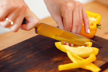 Woman cuts yellow bell pepper for salad on wooden table