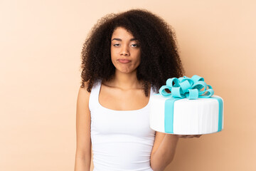 Pastry afro chef holding a big cake isolated on beige background with sad expression