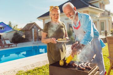 Senior couple grilling meat and corn in their backyard - obrazy, fototapety, plakaty