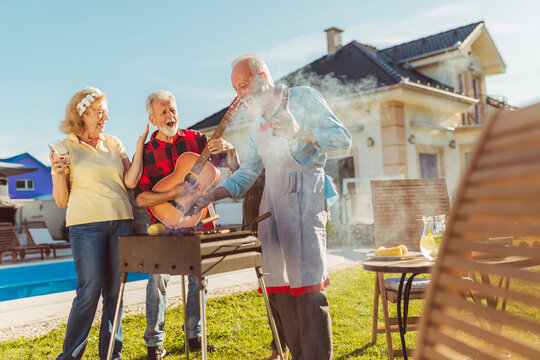 Elderly people playing the guitar and singing while making barbecue