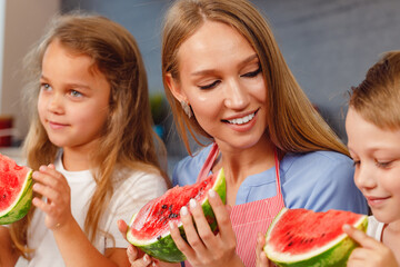 Woman with her daughter and son eating watermelon in kitchen