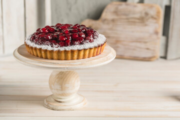 Cherry pie on a white wooden stand on a light background of the kitchen interior.