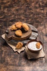 Chicken nuggets on a wooden board with white cream sauce on a dark background.