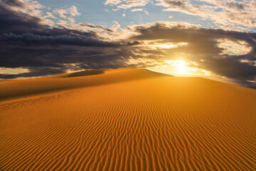 Obraz na płótnie Canvas Sunset over the sand dunes in the desert. Arid landscape of the Sahara desert