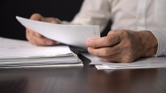 Close-up. Slow motion. A Bundle of Business Papers on the Table. An Elderly Man Holds a Sheet of Paper.