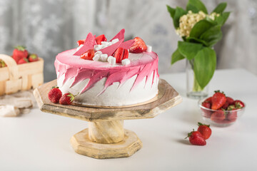 Biscuit cake with strawberry filling and fresh strawberries on a wooden stand on a light background.