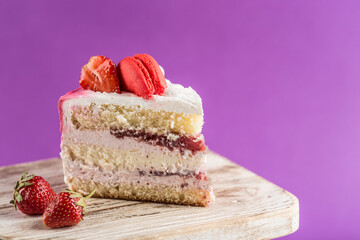 A piece of biscuit cake with strawberry filling and fresh strawberries on a wooden stand on a bright purple background.