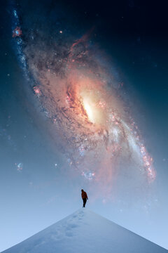 A man standing on snowy hill and looking at a huge spiral galaxy on the night sky
